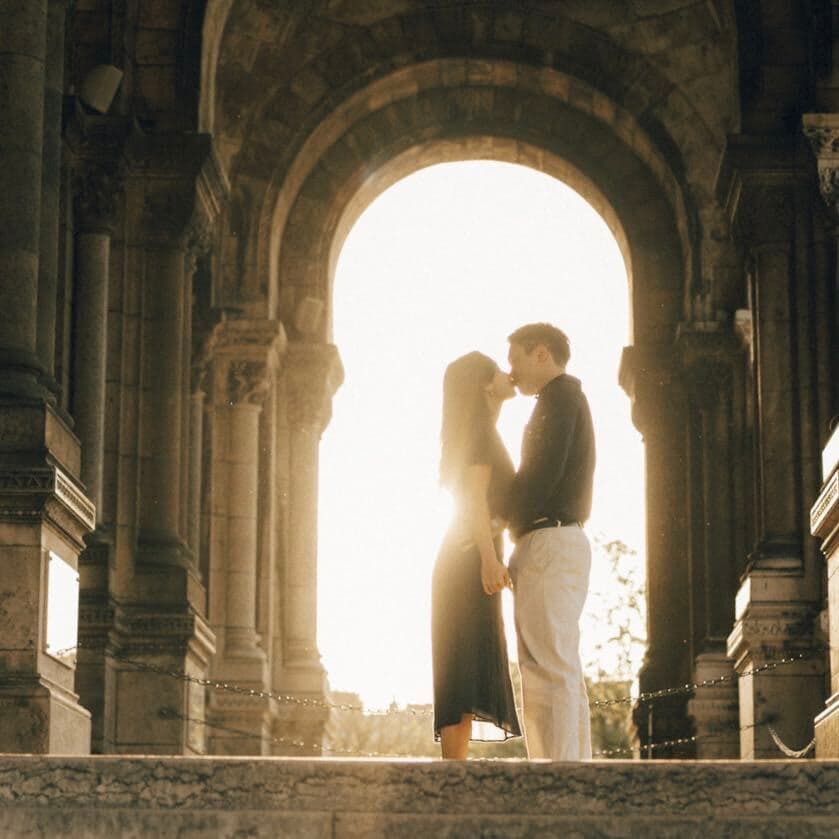Sophia and Ian kissing under a stone arch in the evening sun